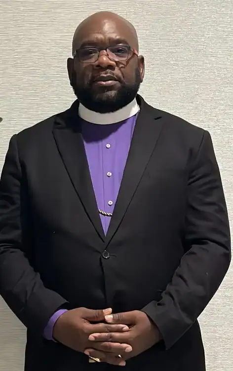 Bishop Jerome M. McLennon in a black suit, purple clergy shirt and white collar
