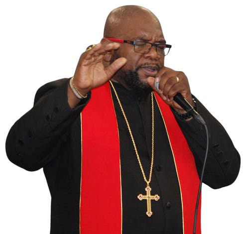 Bishop Jerome M. McLennon preaching in a black robe and red stole, holding a microphone